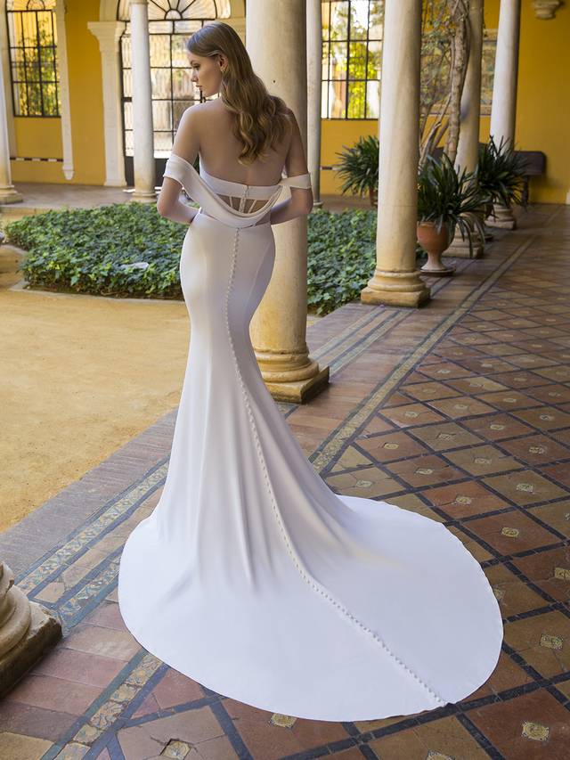Code: Enzoani Blue Payden For our flirty, modern brides, Payden will steal your heart with its crepe mermaid silhouette. This sexy and sleek gown features a one-of-a-kind open corset bodice. The sweetheart neckline is perfected complemented with connecting off-the-shoulder straps for a bold yet romantic look. This sophisticated gown is perfected with buttons lining the gown from top to bottom of the cathedral train.Colour Options: Ivory/Nude OR Ivory/Ivory