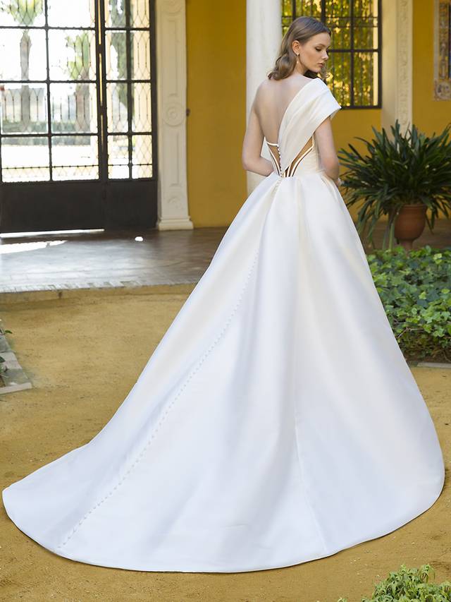 Code: Enzoani Blue Peggy Minimalist bride meets Old Hollywood to create this drop-dead gorgeous ball gown. This Mikado beauty takes front and center stage with a flattering, cinched waistline and ultra-chic, one-shoulder sleeve (and it’s detachable)! For an added touch of glamour and drama, Peggy features an elegant and unique illusion corset back that is truly one-of-a-kind. Colour Options: Ivory/Nude OR Ivory/Ivory