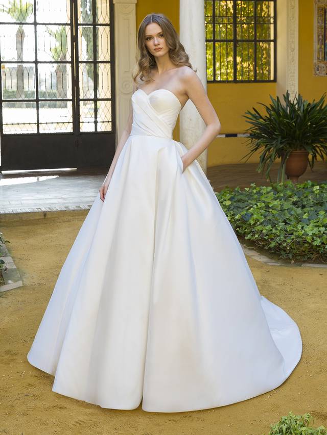 Code: Enzoani Blue Peggy (Without Sleeve) Minimalist bride meets Old Hollywood to create this drop-dead gorgeous ball gown. This Mikado beauty takes front and center stage with a flattering, cinched waistline and ultra-chic, one-shoulder sleeve (and it’s detachable)! For an added touch of glamour and drama, Peggy features an elegant and unique illusion corset back that is truly one-of-a-kind. Colour Options: Ivory/Nude OR Ivory/Ivory