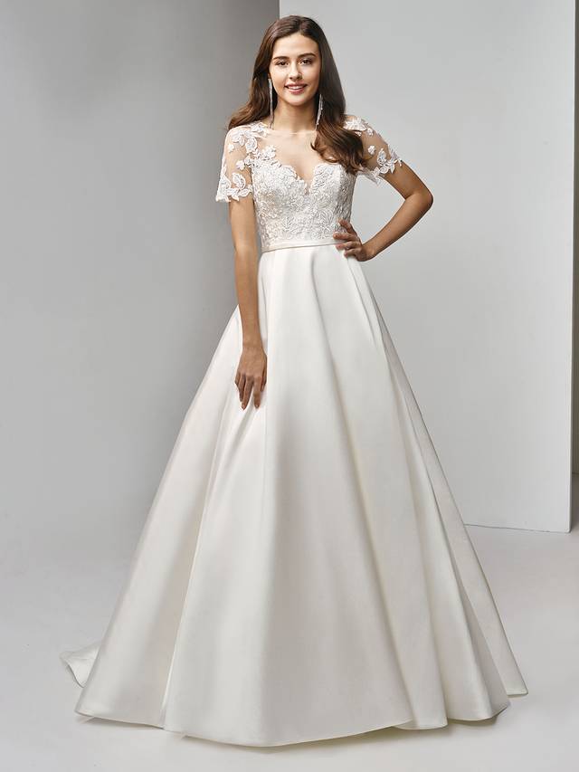 Code: Enzoani Beautiful BT19-15 Code: Enzoani Beautiful BT19-15 Classic with a modern twist -- this full-length, A-line gown is the picture of sweet romance. Delicate embroidered lace is sweet combined with timeless illusion short sleeves and a matching illusion scoop sweetheart neckline. The soft and sleek mikado/satin skirt is accented with a band at the waist to flatter the figure. Finished with covered buttons and an invisible back zipper closure.Colour Options : Ivory
