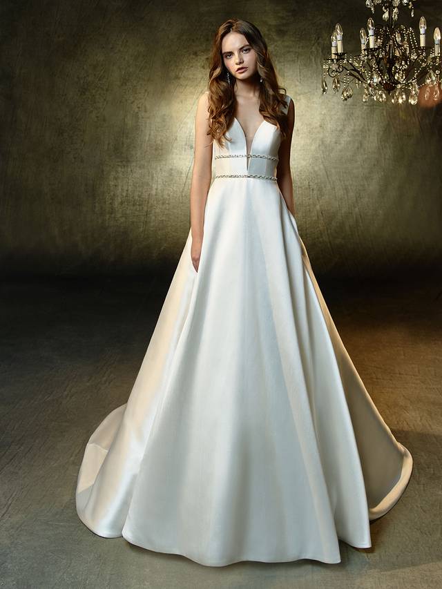 Code: Enzoani Blue Leandra Code: Enzoani Blue Leandra A classic, A-line princess gown with gorgeous, contemporary updates. This full-length, sleek mikado gown features a plunging illusion sweetheart neckline that meets two sparkling, thin rhinestone bands to create the most figure-flattering, waist-cinching effect. A low, open back provides even more modern sexiness.Cololur Options : Ivory/Nude OR Ivory/Ivory