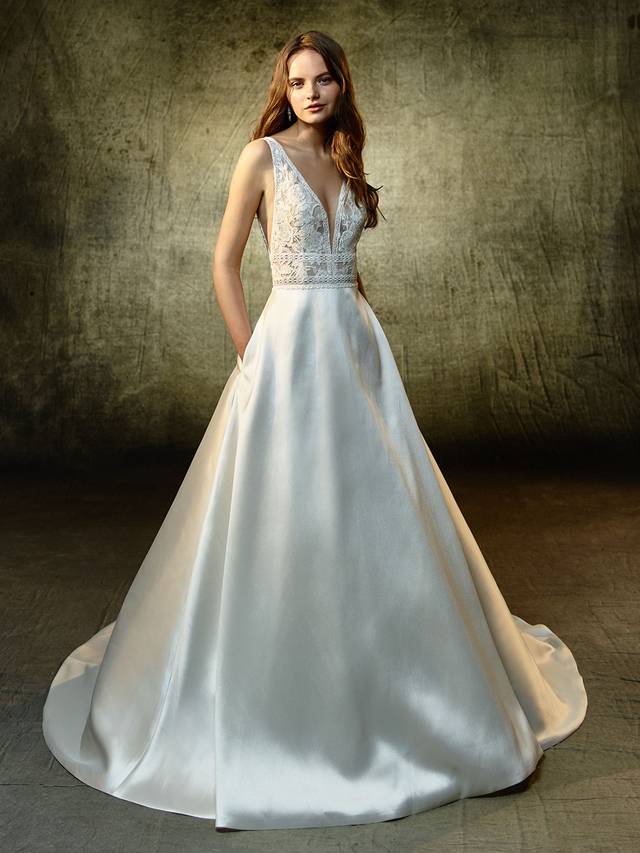 Code: Enzoani Blue Lilybeth Code: Enzoani Blue Lilybeth Equal parts classic and modern, this full-length, A-line gown balances a contemporary embroidered lace and chantilly lace bodice and a sleek, chic mikado skirt. A deep V-neckline is gorgeously trimmed with lace to match the lace bands cinching the waist. The low, open back is perfectly framed with lace straps, while covered buttons trailing down the length of the skirt and train provide the sweet, eye-catching finishing detail.Colour Options : Ivory/Nude OR Ivory/Ivory