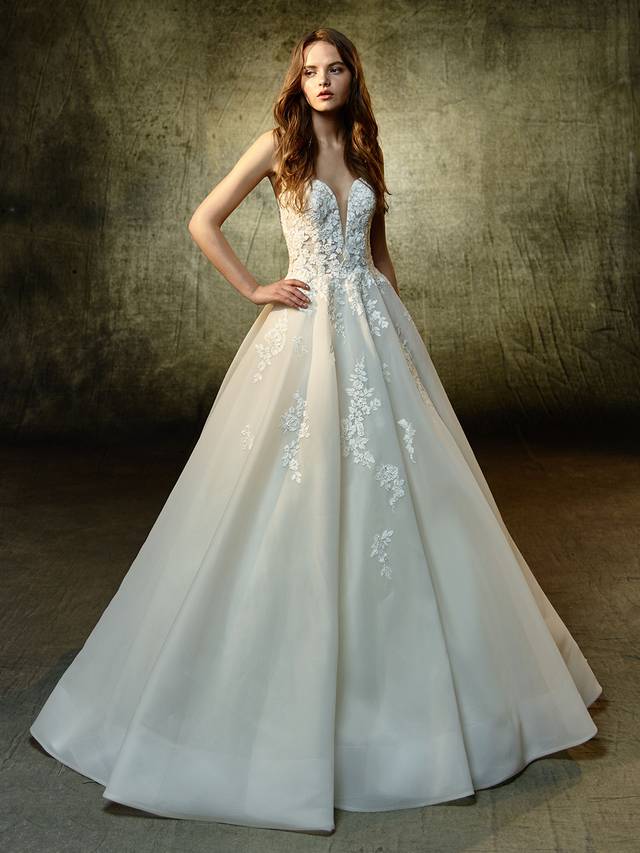 Code: Enzoani Blue Lyvia - IN STUDIO Code: Enzoani Blue Lyvia - IN STUDIO Polished, pretty, and picture-perfect. This full A-line gown features a plunging strapless sweetheart neckline illusion bodice with sparkling beaded, embroidered lace sprinkling down to the dreamy organza skirt. A complementary illusion lace back is finished with an invisible back zipper closure.Colour Options : Dark Ivory/Ivory OR Ivory/Ivory