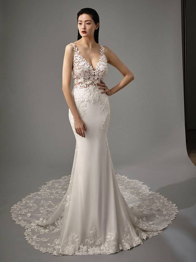 Code: Enzoani Blue - Malia Code: Enzoani Blue - Malia Become mesmerized with the Malia gown. Modern and sultry, this full length mermaid gown offers an enviable floral train. Delicate floral lace appliques are placed onto the bodice cascading down to the hips. Stretch georgette harmoniously compliments the lace as it is then ruched in the back of the gown. Finished with a playful low v-back, covered buttons, and an invisible zipper.Colour Options: Ivory