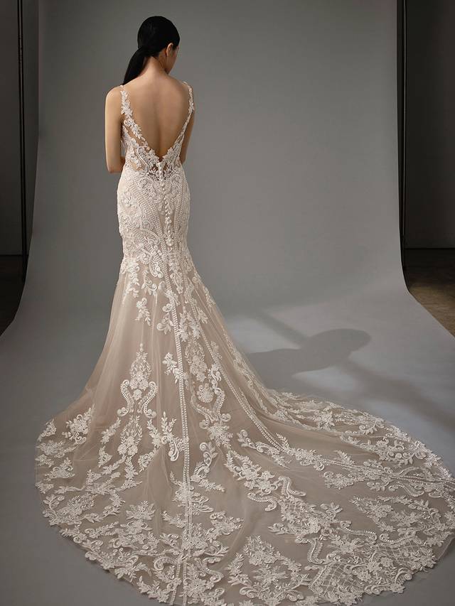 Code: Enzoani Blue - Marianna Code: Enzoani Blue - Marianna Vintage and classic meets modern and sultry. Regal lace covers this mermaid gown as it is carefully placed between the bodice, tulle skirt and train. Its low V-neckline is complemented by its low, sultry V-back, complete with a trail of covered buttons. A lace train finishes the look for a modern, romantic touch. Pair this gown with its veil.Colour Options: Ivory/Beige/Nude OR Ivory/Ivory/Ivory OR Ivory/Ivory/Nude OR Ivory/Nude/Nude