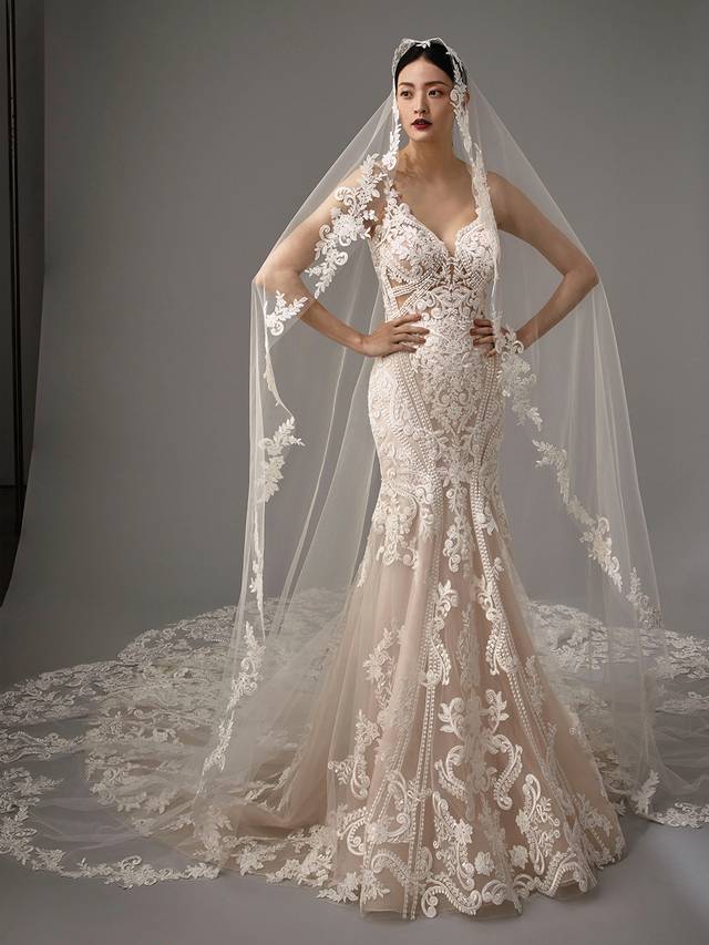 Code: Enzoani Blue - Marianna with Veil Code: Enzoani Blue - Marianna with Veil Vintage and classic meets modern and sultry. Regal lace covers this mermaid gown as it is carefully placed between the bodice, tulle skirt and train. Its low V-neckline is complemented by its low, sultry V-back, complete with a trail of covered buttons. A lace train finishes the look for a modern, romantic touch. Pair this gown with its veil.Colour Options: Ivory/Beige/Nude OR Ivory/Ivory/Ivory OR Ivory/Ivory/Nude OR Ivory/Nude/Nude