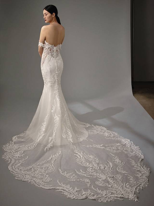 Code: Enzoani Blue - Martha Code: Enzoani Blue - Martha An alluring lace bodice with a sweetheart neckline and soft stretch georgette make the perfect combination for this elegant mermaid gown. Detachable off-the-shoulder sleeves are added for an extra romantic touch. A subtle lace illusion side panel adds a touch of playfulness. Covered buttons trail from the back to the end of its extravagant train.Colour Options: Ivory/Nude OR Ivory/Ivory,