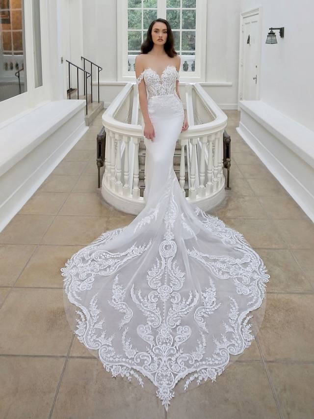 Code: Enzoani Blue - Martha - IN STUDIO Code: Enzoani Blue - Martha - IN STUDIO An alluring lace bodice with a sweetheart neckline and soft stretch georgette make the perfect combination for this elegant mermaid gown. Detachable off-the-shoulder sleeves are added for an extra romantic touch. A subtle lace illusion side panel adds a touch of playfulness. Covered buttons trail from the back to the end of its extravagant train.Colour Options: Ivory/Nude OR Ivory/Ivory