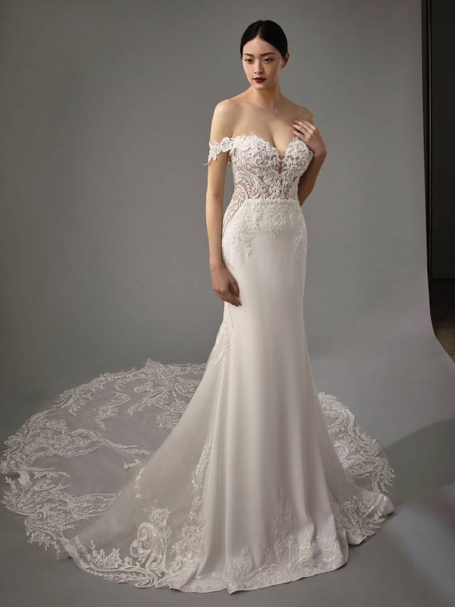 Code: Enzoani Blue - Martha Code: Enzoani Blue - Martha An alluring lace bodice with a sweetheart neckline and soft stretch georgette make the perfect combination for this elegant mermaid gown. Detachable off-the-shoulder sleeves are added for an extra romantic touch. A subtle lace illusion side panel adds a touch of playfulness. Covered buttons trail from the back to the end of its extravagant train. Colour Options: Ivory/Nude OR Ivory/Ivory,