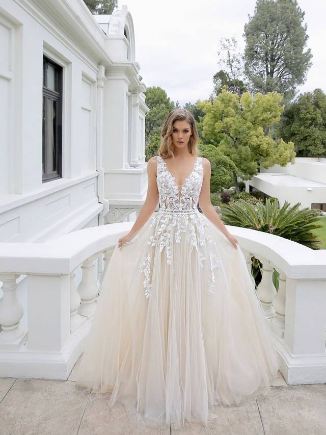 Code: Enzoani Blue - Mikayla - IN STUDIO Code: Enzoani Blue - Mikayla - IN STUDIO Sweet and ethereal, this A-line gown features a plunging neckline on a gorgeous chantilly lace bodice. Lace continues to cascade gently onto dreamy tulle layers of the skirt. Whimsical and romantic, Mikayla also features an open V-back with covered buttons and an invisible zipper closure.Colour Options: Ivory/Beige/Nude OR Ivory/Ivory/Ivory OR Ivory/Ivory/Nude