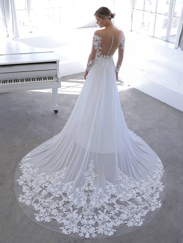 Code: Blue By Enzoani Nandana Code: Blue By Enzoani Nandana You will float down the aisle in this ethereal A-line gown! NANDANA features elegant, long tulle sleves with captivating 3D floral cotton lace and a lightweight chiffon skirt. The illusion tulle bodice gives you the appearance that this is an off-the-shoulder style. The back features covered buttons that lead to an invisible zipper finished with hand placed floral appliques along the train. Colour Options: Ivory/Nude OR Ivory/Ivory