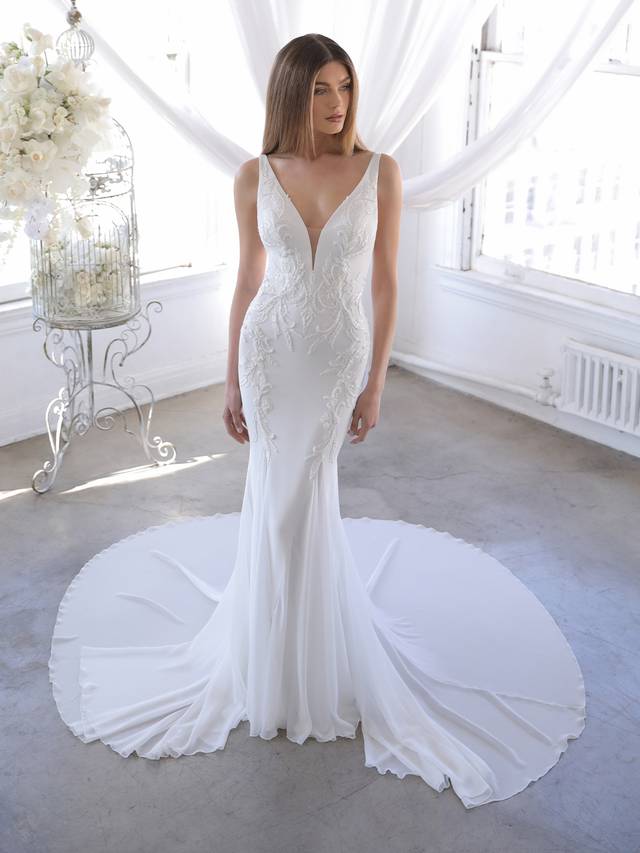 Code: Blue By Enzoani Olivette Code: Blue By Enzoani Olivette This mermaid gown is all about clean lines and sleek sophistication with a twist – elegant embroidered lace beautifully trails down from the sexy plunging V-neckline and weaves throughout the illusion back for a cohesive look. The light-as-air chiffon and tulle skirt is modern and minimalist, perfect for brides who want an effortlessly glam look.Colour Options: Ivory/Nude OR Ivory/Ivory