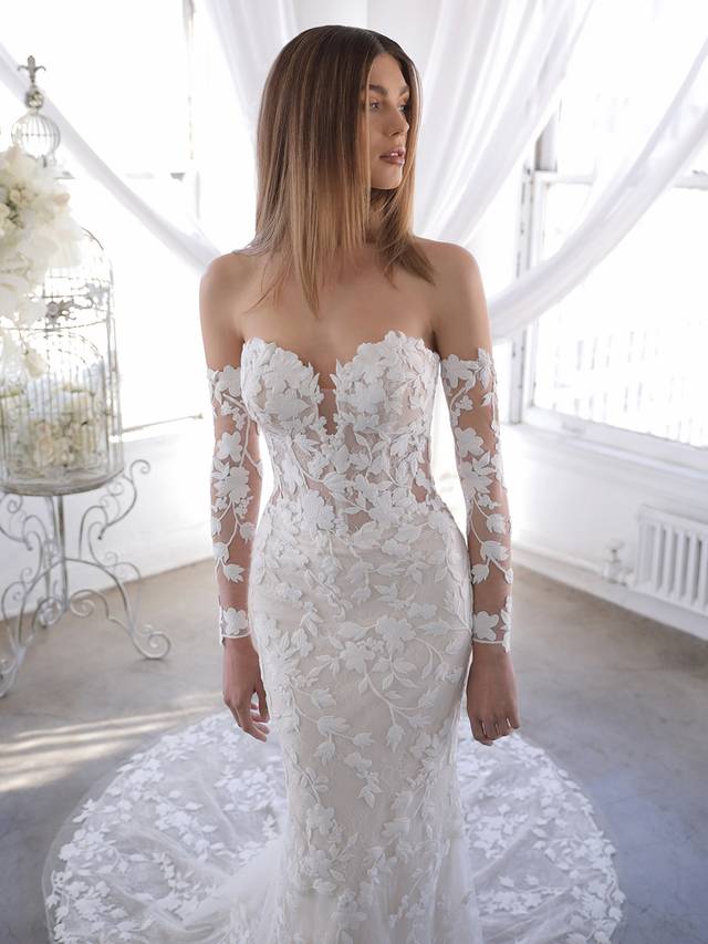 Code: Blue By Enzoani Orrie (with sleeves) Code: Blue By Enzoani Orrie (with sleeves) Orrie is the answer for our brides who love the Naroza but want the option to completely remove the long off-shoulder sleeves. Our beloved thick embroidered floral lace is front and center on this gown with a deep sweetheart neckline and eye-catching illusion corset-style back with covered buttons.Colour Options: Ivory/Sand/Nude OR Ivory/Ivory/Nude OR Ivory/Nude/Nude OR Ivory/Ivory/Ivory