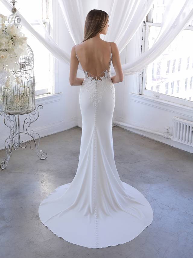 Code: Blue By Enzoani Ozalea Code: Blue By Enzoani Ozalea Ozalea is for the modern bride who wants the best of both worlds – clean and simple but also dramatic and showstopping. A detachable tulle and lace train is perfect for added splendor for the ceremony and wedding photos, and can be removed to reveal a sleek and elegant stretch georgette silhouette. Thick floral embroidered lace provides gorgeous detailing to accentuate the sexy plunging V-neckline and low illusion back.Colour Options: Ivory/Nude OR Ivory/Ivory