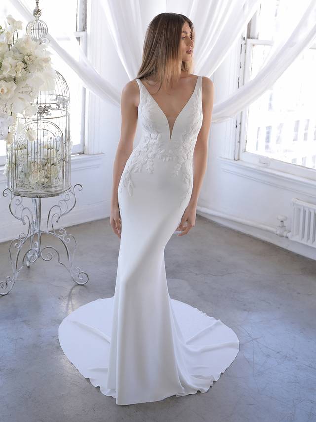 Code: Blue By Enzoani Ozalea Code: Blue By Enzoani Ozalea Ozalea is for the modern bride who wants the best of both worlds – clean and simple but also dramatic and showstopping. A detachable tulle and lace train is perfect for added splendor for the ceremony and wedding photos, and can be removed to reveal a sleek and elegant stretch georgette silhouette. Thick floral embroidered lace provides gorgeous detailing to accentuate the sexy plunging V-neckline and low illusion back.Colour Options: Ivory/Nude OR Ivory/Ivory