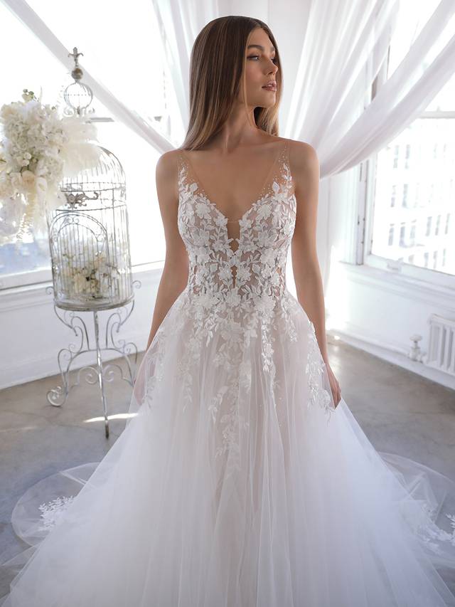 Code: Enzoani Blue Olani - ARRIVING SOON Code: Enzoani Blue Olani - ARRIVING SOON A delicate and sexy illusion lace back and V-neckline adorned with beautiful floral embroidered lace gorgeously trickles down to the dreamiest organza, glitter tulle and tulle skirt. The gown will sparkle and shine at every turn, creating the most heavenly effect. Romantic floral lace appliques peeking through the ethereal A-line skirt add even more playful beauty for brides as they walk down the aisle. Colour Options: Ivory/Nude/Nude OR Ivory/Ivory/Nude OR Ivory/Ivory/Ivory