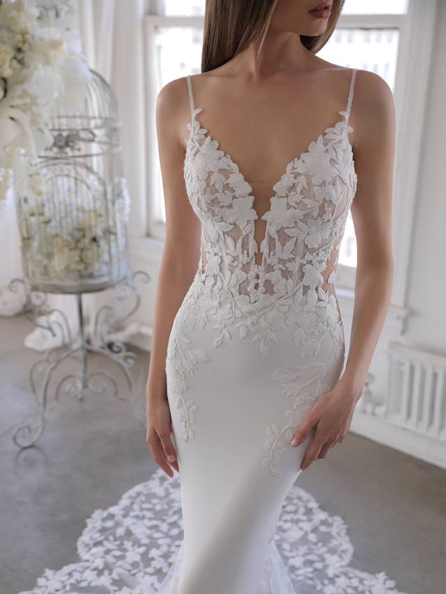 Code: Enzoani Blue Oliviana - ARRIVING SOON Code: Enzoani Blue Oliviana - ARRIVING SOON This gorgeous mermaid gown features the sought-after thick floral embroidered lace of bestselling styles on a plunging illusion sweetheart neckline bodice with sweet spaghetti straps. The illusion lace back is sure to keep all eyes on the bride, especially with the lace beautifully cascading down the softest stretch georgette and tulle skirt featuring a signature Enzoani scalloped lace train. Colour Options: Ivory/Nude OR Ivory/Ivory