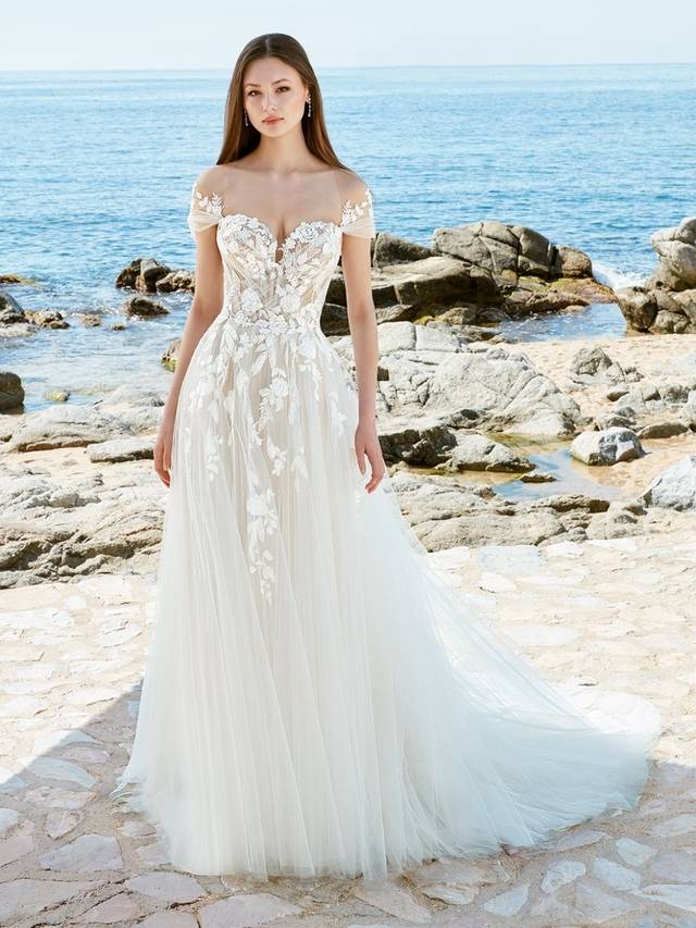 Code: Love By Enzoani Aisha Code: Love By Enzoani Aisha It’s truly modern romance. The full light layers of different textures of glitter tulle and organza exude ethereal appeal. This gown features a plunging sweetheart neckline, open back details, an intricately embellished structured bodice with soft net artfully pleated, and a full, subtly shimmery skirt. AISHA is designed to make a statement. Add the matching detachable off-the-shoulder sheer lace sleeves for a more classic look.Colour Options: Ivory/Nude OR Ivory/Ivory