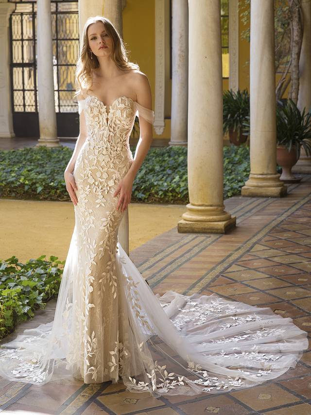 Code: Blue By Enzoani Paloma Code: Blue By Enzoani Paloma Picture-perfect romance is easily achieved with this figure-hugging mermaid gown, which is for the bride who wants to show off those curves and sexy sophistication. It is designed with soft and romantic detachable off-shoulder tulle straps on a V-plunge illusion sweetheart neckline bodice. This bespoke thick cotton floral lace delicately embellishes the bodice to shape your torso and frame the illusion corset-style back featuring covered buttons for a glamorous, modern touch, drawing the eye down to the breathtaking, cascading train with just the right amount of dreamy lace detailing.Colour Options: Ivory/Nude/Nude OR Ivory/Ivory/Nude OR Ivory/Ivory/Ivory OR Ivory/Sand/Nude