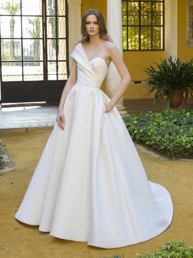 Code: Blue By Enzoani Peggy Code: Blue By Enzoani Peggy Minimalist bride meets Old Hollywood to create this drop-dead gorgeous ball gown. This Mikado beauty takes front and center stage with a flattering, cinched waistline and ultra-chic, one-shoulder sleeve (and it’s detachable)! For an added touch of glamour and drama, Peggy features an elegant and unique illusion corset back that is truly one-of-a-kind.Colour Options: Ivory/Nude OR Ivory/Ivory