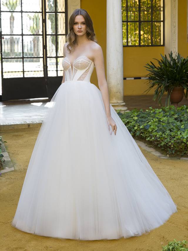 Code: Blue By Enzoani Penina Code: Blue By Enzoani Penina This stunning look is the perfect balance between simplicity and whimsy. Featuring a V-plunge illusion sweetheart neckline, a boned ivory padded corset-style bodice, and combined with dazzling beaded texture sheer panels, it lends a modern edge and eye-catching effects to this fairytale-like tulle ball gown.Colour Options: Ivory/Nude OR Ivory/Ivory