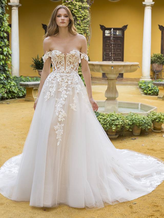 Code: Blue By Enzoani Petunia Code: Blue By Enzoani Petunia Sweet and ethereal, this lavish, full A-line bridal gown features a V-plunge illusion sweetheart neckline on a gorgeous shimmer beaded lace bodice and 3D floral embroidery off-the-shoulder straps. The whimsical appliques adorning the corset-style bodice gently trickle down to the lush skirt. This gown is perfect for the modern bride who wants both exquisite detailing and unique versatility. Ivory/Nude/Nude OR Ivory/Ivory/Ivory OR Ivory/Sand/Nude