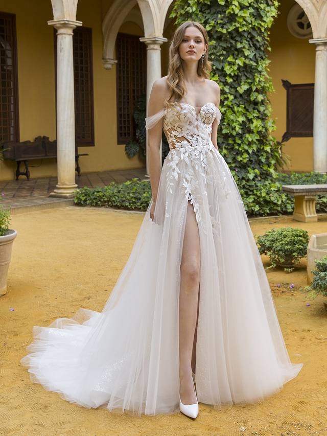 Code: Blue By Enzoani Pia Code: Blue By Enzoani Pia As sweet as can be with an undeniable allure, this modern A-line silhouette is sure to captivate. It features custom-made, vine-like 3D motif appliques placed along the V-plunge illusion bodice and floating down the sparkle skirt, paired with an asymmetrical off-the shoulder tulle wrap (that is detachable!) Exquisite detailing and tulle form a cascading, dreamy skirt. The soft layers of tulle, sequins scattered net and sheer gauze brings this slit gown even more sexy sophistication, while a lace-framed, corset-style back is the sweetest detail to finish off the look.Colour Options: Ivory/Ivory/Nude OR Ivory/Ivory/Ivory OR Ivory/Sand/Nude