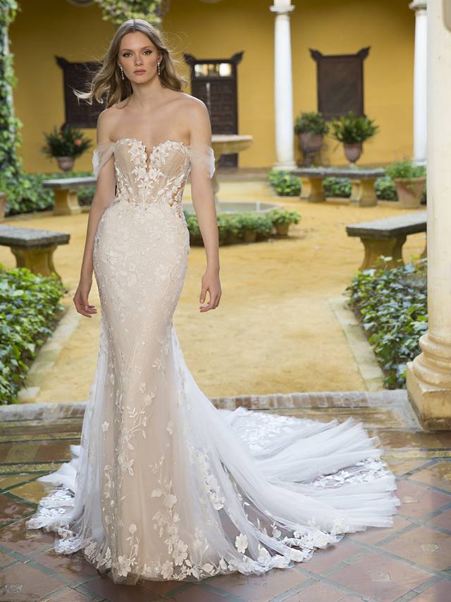 Code: Blue By Enzoani Prisha Code: Blue By Enzoani Prisha Like floating on clouds in our dreamy Prisha. This breathtaking mermaid gown features floral cotton lace that wraps around the silhouette of the gown. The laser cut floral lace balances perfectly with the detailed tulle bodice emphasizing the plunging sweetheart neckline. Change up this bridal look by removing the lovely detachable tulle sleeves for a more fun and flirtier look.Colour Options: Ivory/Nude/Nude OR Ivory/Ivory/Nude OR Ivory/Ivory/Ivory OR Ivory/Sand/Nude