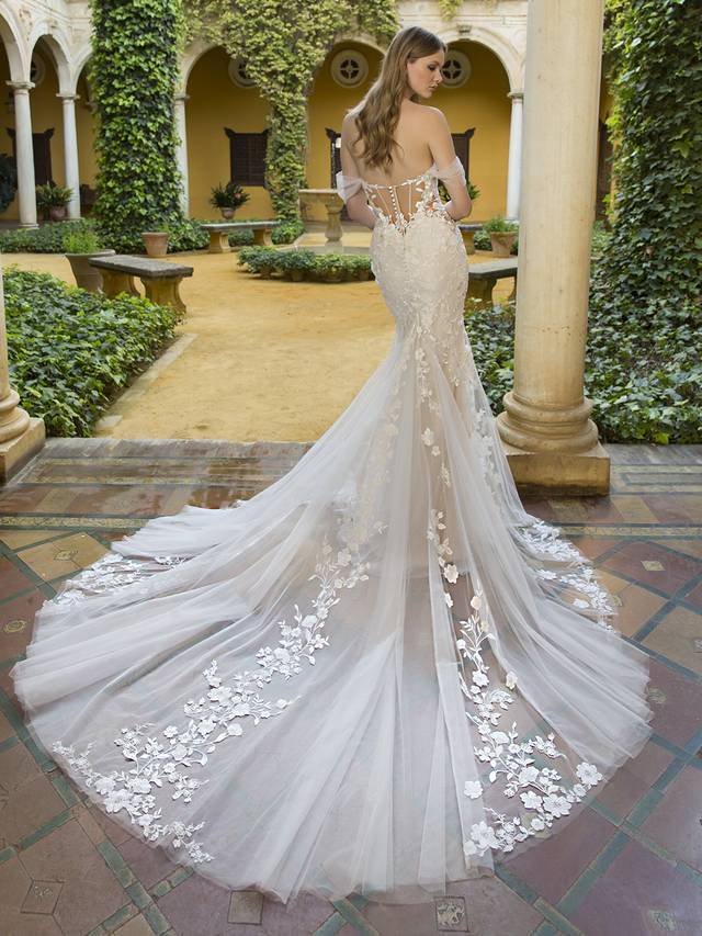 Code: Blue By Enzoani Prisha Code: Blue By Enzoani Prisha Like floating on clouds in our dreamy Prisha. This breathtaking mermaid gown features floral cotton lace that wraps around the silhouette of the gown. The laser cut floral lace balances perfectly with the detailed tulle bodice emphasizing the plunging sweetheart neckline. Change up this bridal look by removing the lovely detachable tulle sleeves for a more fun and flirtier look.Colour Options: Ivory/Nude/Nude OR Ivory/Ivory/Nude OR Ivory/Ivory/Ivory OR Ivory/Sand/Nude