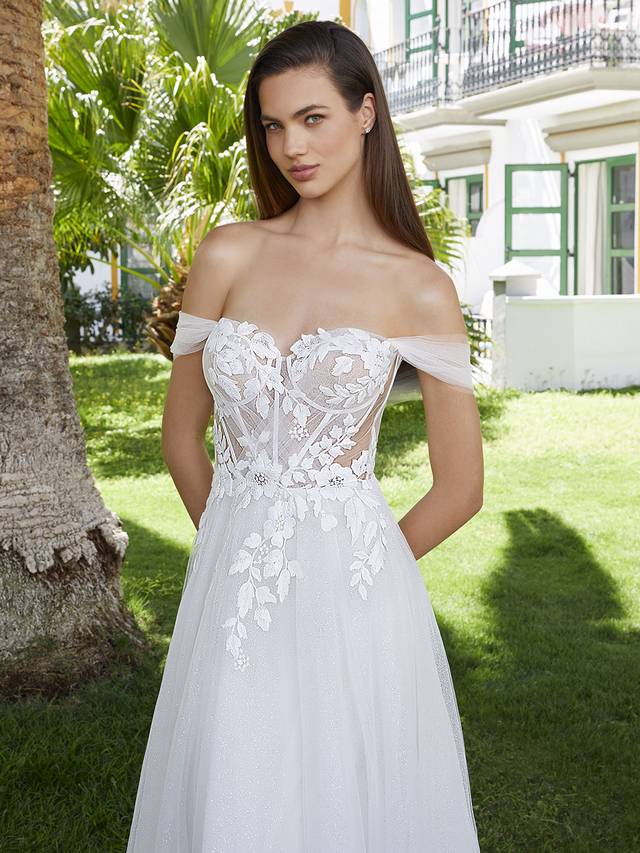 Code: Love By Enzoani Bernadine Code: Love By Enzoani Bernadine BERNADINE effortlessly exudes romance. The soft sweetheart neckline is elegantly balanced with dreamy off-the-shoulder tulle sleeves, a sexy illusion corset style bodice with exposed boning and delicately scattered floral embroidered lace that drapes onto an ethereal glitter tulle skirt. The tulle draping detail across the appliques adds even more eye-catching flair to this uniquely sweet and modern gown. Colour Options: Ivory/Beige/Nude OR Ivory/Ivory/Ivory OR Ivory/Ivory/Nude