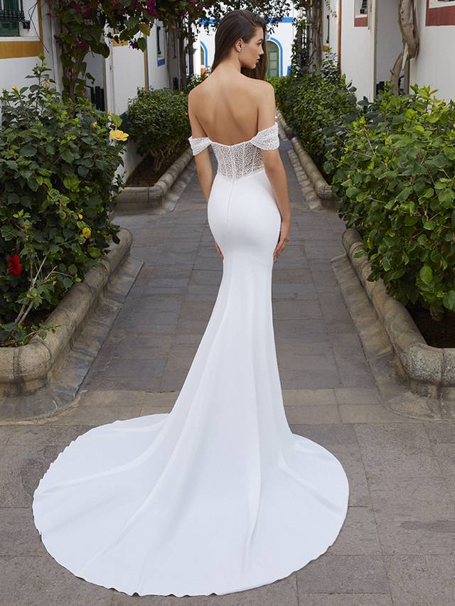 Code: Love By Enzoani Blanca Code: Love By Enzoani Blanca Sexy, simple and striking. BLANCA is a perfect balance of minimalism and glamour. Intricate beaded tulle lace brings detailed texture to the corset style bodice of the gown. A mix of exposed boning details, a plunging illusion sweetheart neckline with illusion side cut-outs, and embellished off-the-shoulder sleeves blend together perfectly to create the most flattering and eye-catching silhouette. A figure-hugging, sleek and soft stretch georgette skirt balances with the drama of the bodice perfectly.Colour Options: Ivory/Nude OR Ivory/Ivory