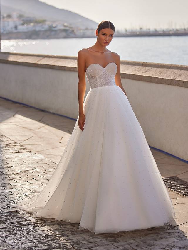 Code: Moonlight Tango T984 Code: Moonlight Tango T984 A breathtaking wedding dress truly designed for the queen in us all. This dreamy ball gown flows from the natural waist with layers of wispy tulle and dotted throughout the skirt and through its charming sweep train are glistening pearls that catch the light with your every move.Make an effortless transformation with a detachable off-the-shoulder jacket constructed with more airy ruched tulle and matching pearls.Colour Option: Ivory