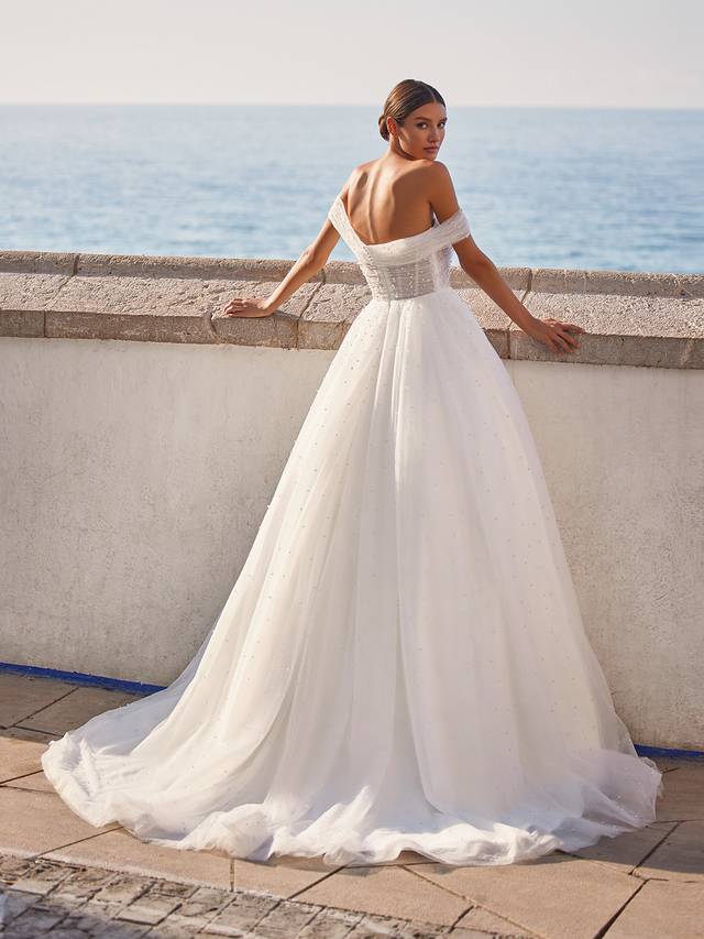 Code: Moonlight Tango T984 Code: Moonlight Tango T984 A breathtaking wedding dress truly designed for the queen in us all. This dreamy ball gown flows from the natural waist with layers of wispy tulle and dotted throughout the skirt and through its charming sweep train are glistening pearls that catch the light with your every move.Make an effortless transformation with a detachable off-the-shoulder jacket constructed with more airy ruched tulle and matching pearls.Colour Option: Ivory
