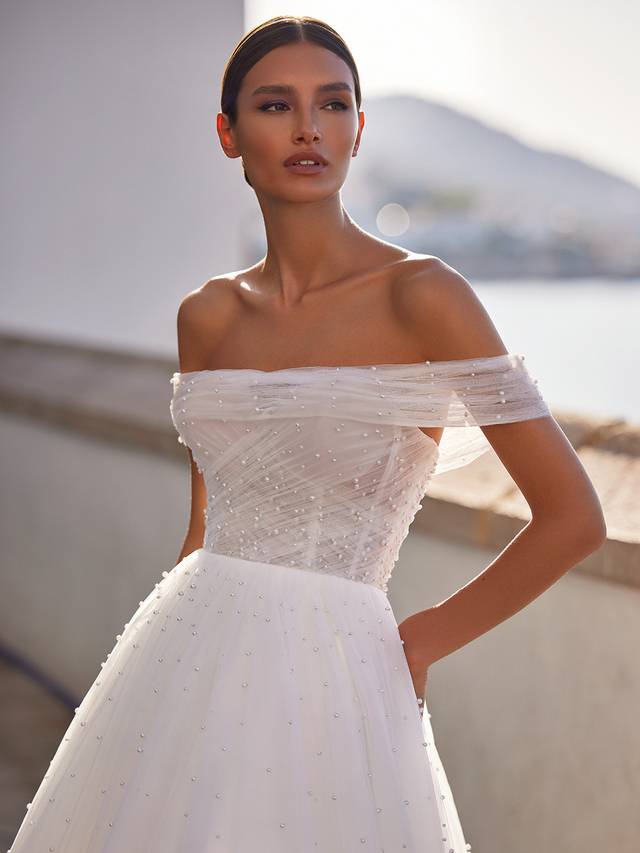Code: Moonlight Tango T984 Code: Moonlight Tango T984 A breathtaking wedding dress truly designed for the queen in us all. This dreamy ball gown flows from the natural waist with layers of wispy tulle and dotted throughout the skirt and through its charming sweep train are glistening pearls that catch the light with your every move.Make an effortless transformation with a detachable off-the-shoulder jacket constructed with more airy ruched tulle and matching pearls.Colour Option: Ivory